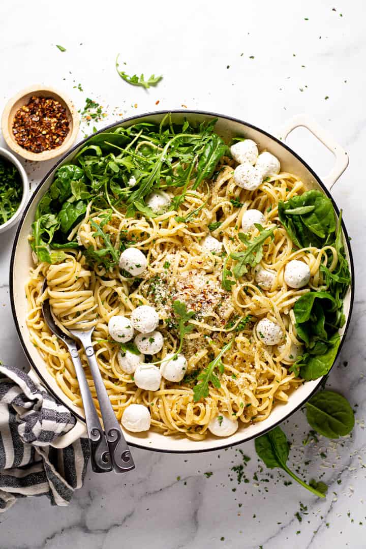 Overhead shot of a pan of garlic butter noodles garnished with Parmesan arugula and fresh mozzarella