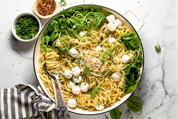 Overhead shot of a pan of garlic butter noodles garnished with Parmesan arugula and fresh mozzarella