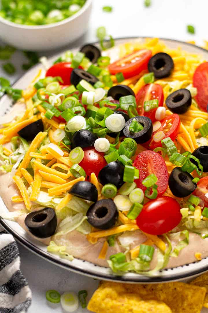 Close up shot of taco dip on a black and white plate served with tortilla chips