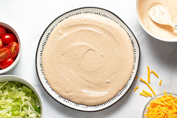 Taco dip being assembled on a black and white serving platter