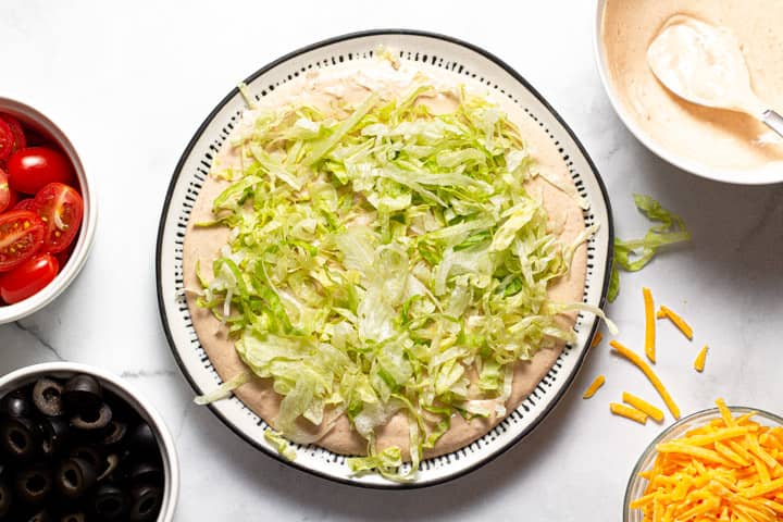 Taco dip being assembled on a black and white serving platter