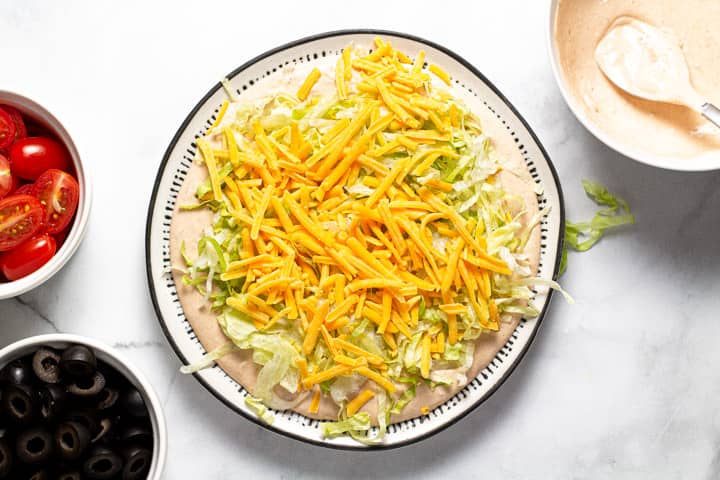 Taco dip being assembled on a black and white serving platter