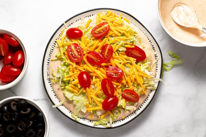 Taco dip being assembled on a black and white serving platter