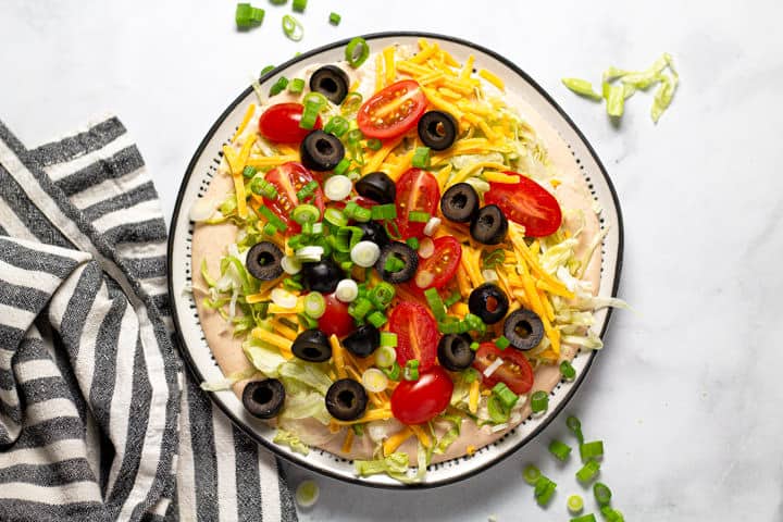 Overhead shot of taco dip on a black and white plate sitting on a white marble counter top