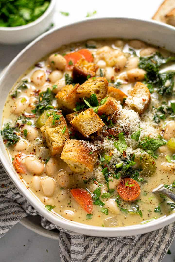 Close up shot of a bowl of creamy vegan white bean soup with croutons and chopped parsley 