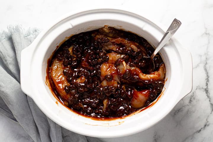 Overhead shot of a white slow cooker with BBQ chicken and beans in it