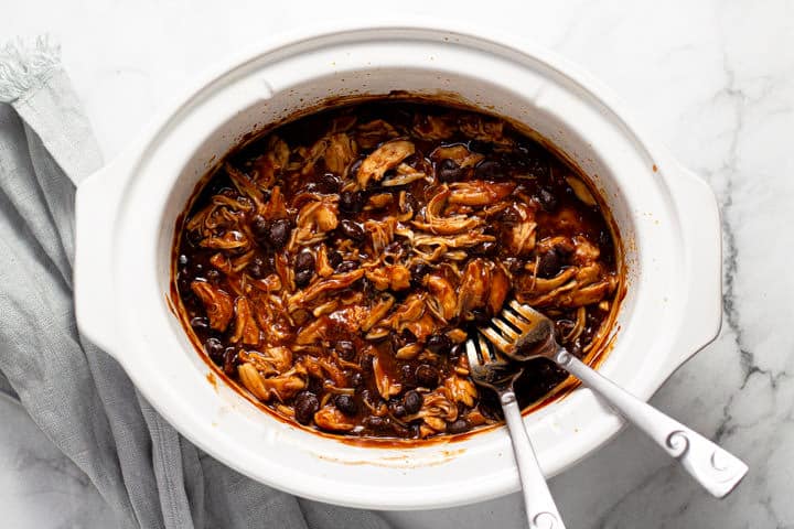 Overhead shot of a white slow cooker with shredded BBQ chicken and beans in it