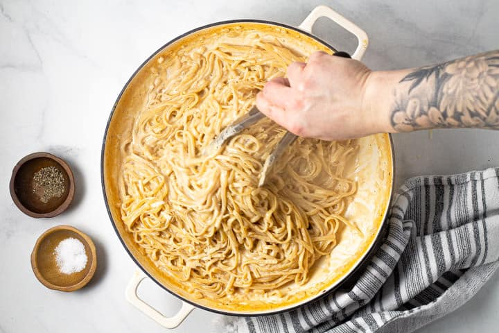 Tongs tossing a large pot of alfredo pasta