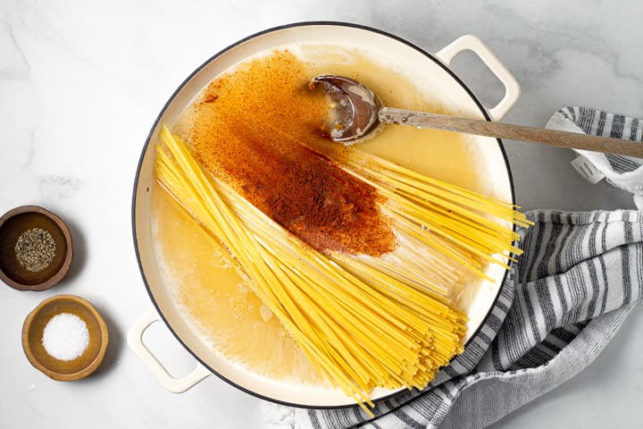 A large white pot filled with noodles broth and chipotle powder