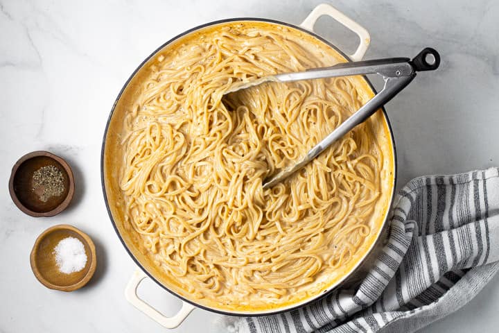 Large white pot filled with one pot alfredo and a pair of tongs