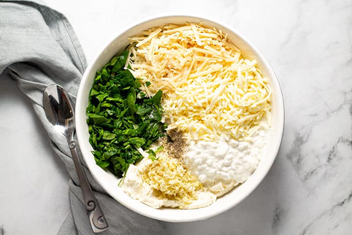 Large white bowl filled with ingredients to fill spinach lasagna roll ups