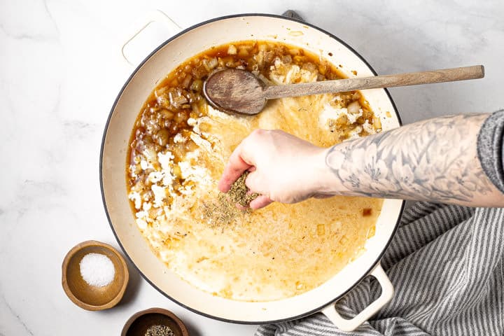 Dried herbs being added to pasta sauce in a large white pot