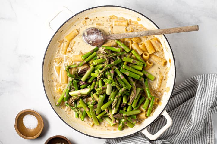 Chopped asparagus on top of cooked rigatoni in a large white pot
