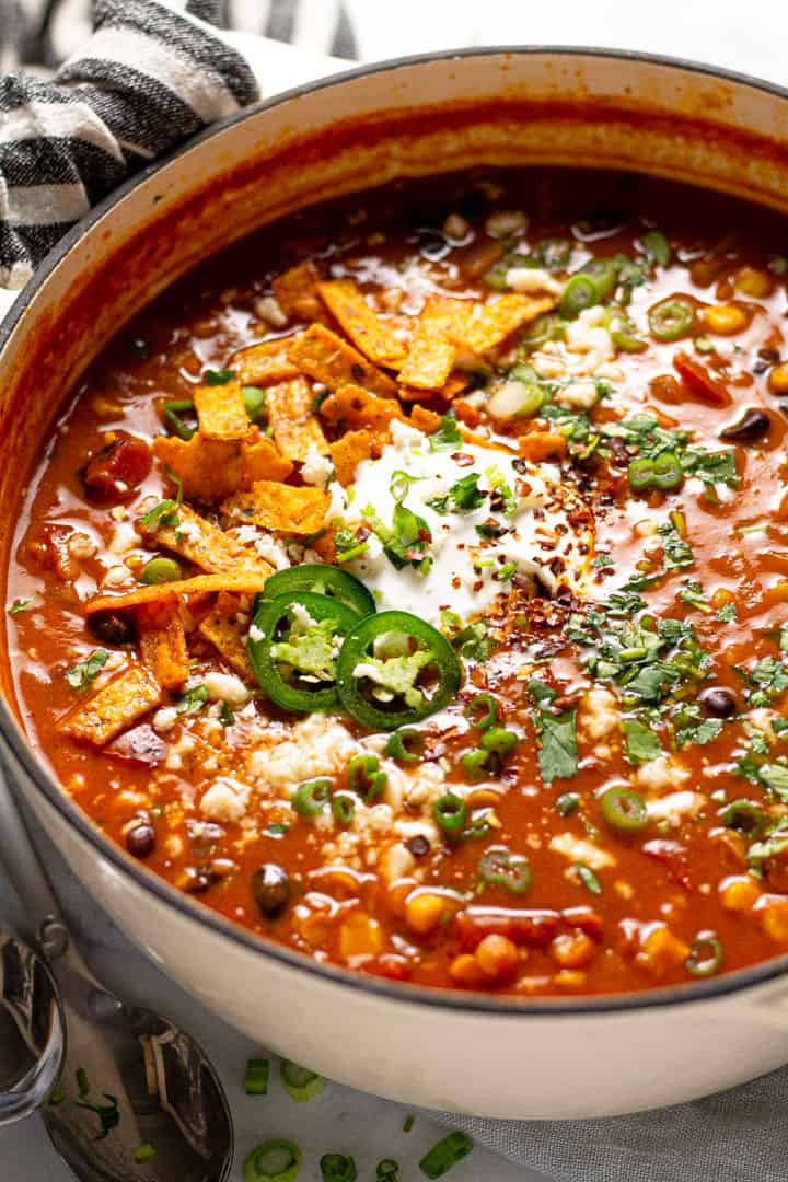 Close up shot of a large pot of vegan lentil tortilla soup garnished with fresh chopped cilantro 