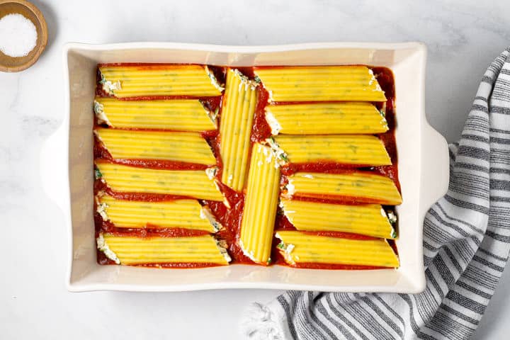 Filled manicotti noodles in a 9x13 pan filled with sauce