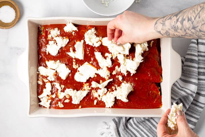 Two hands breaking up fresh mozzarella and placing it on top of manicotti