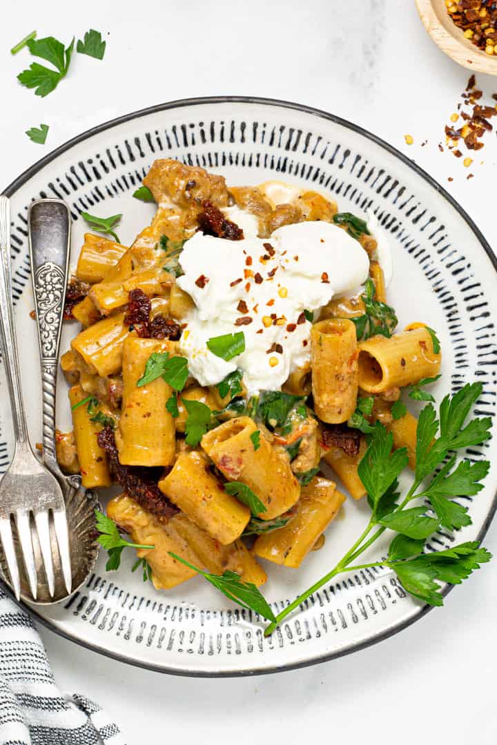 Black and white plate filled with sausage rigatoni garnished with fresh parsley