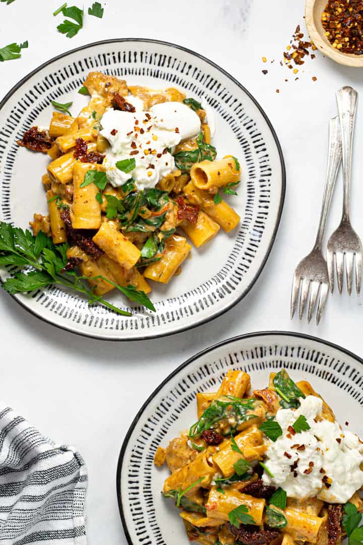 Two black and white plate filled with sausage rigatoni garnished with fresh parsley