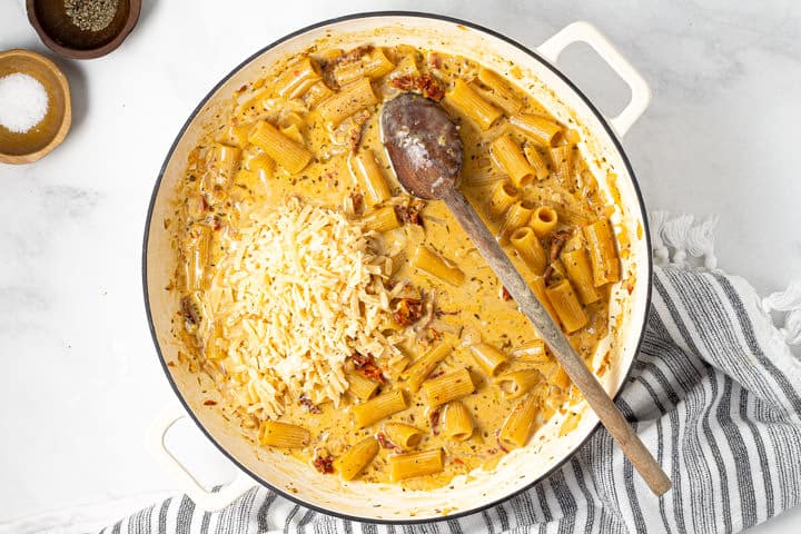 Large white pot with shredded Parmesan and saucy rigatoni in it