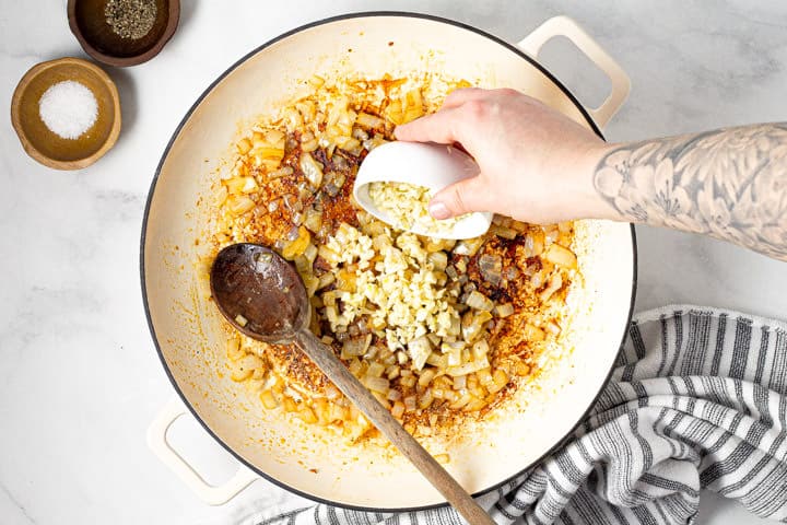 Large white pot with sauteed onions and garlic being added to it