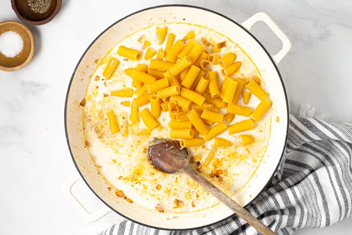 Uncooked rigatoni in a large white pan of broth and half and half