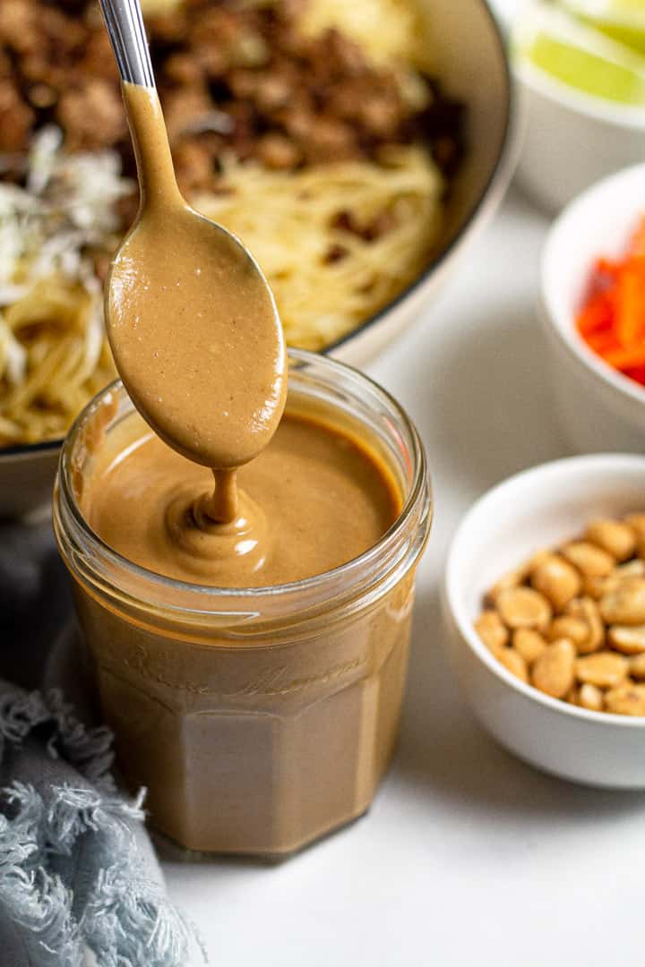 Creamy peanut sauce dripping off a spoon over a jar of the sauce
