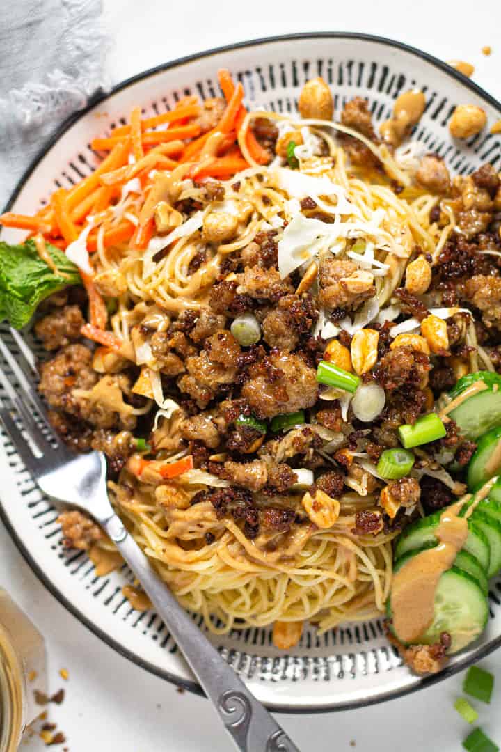 Overhead shot of a black and white plate with Thai pork noodles garnished with sliced green onions