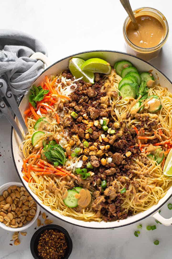 Overhead shot of a large white pot filled with Thai pork noodles and fresh veggies