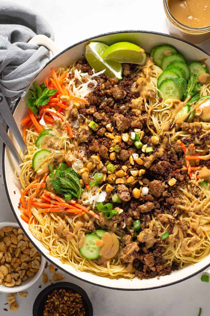 Overhead shot of a large white pot filled with Thai pork noodles and fresh veggies