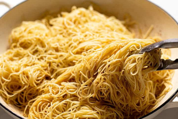 Angel hair pasta being tossed in a large white pot