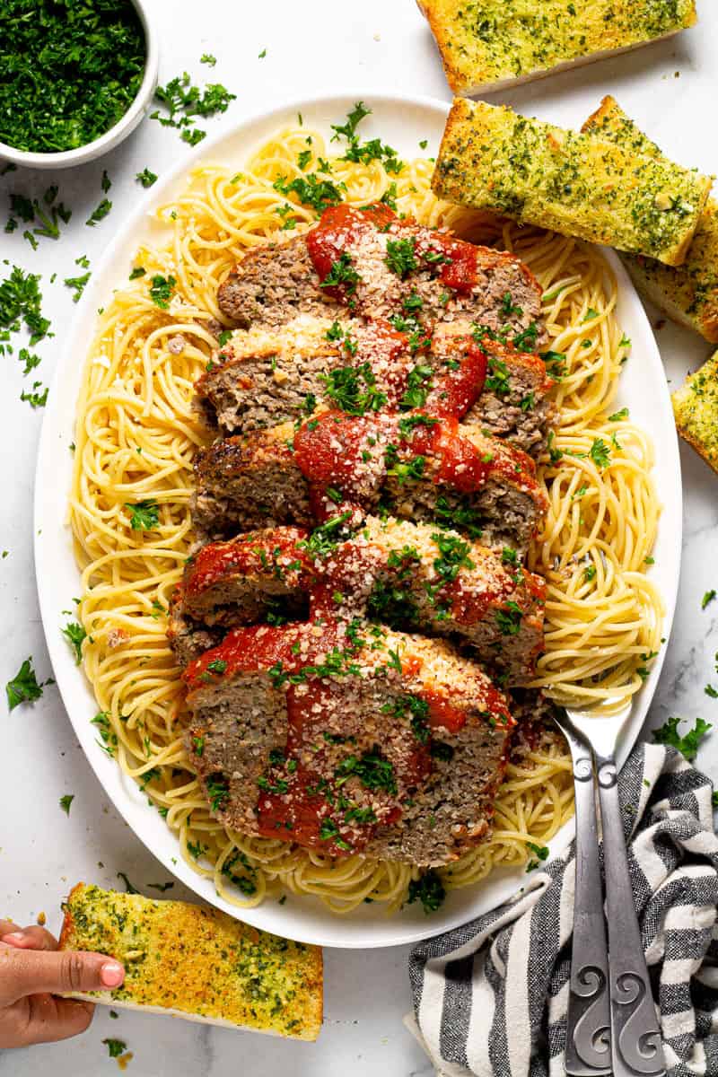 Large white platter with an Italian meatloaf sliced on top of a bed of spaghetti noodles 
