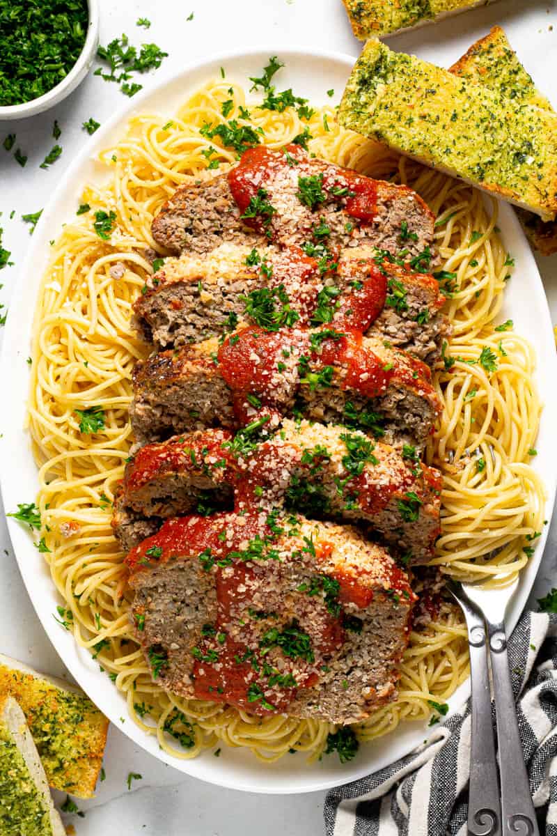 Large white platter with an Italian meatloaf sliced on top of a bed of spaghetti noodles 