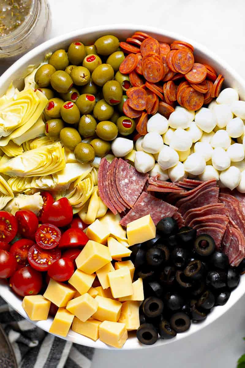 Overhead shot of a white bowl filled with the ingredients for antipasto pasta salad