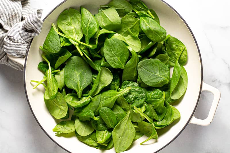 Overhead shot of a baking dish filled with fresh spinach leaves