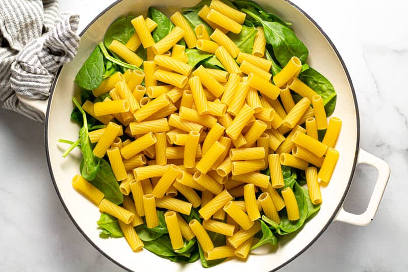 Overhead shot of a baking dish filled with fresh spinach leaves and uncooked noodles