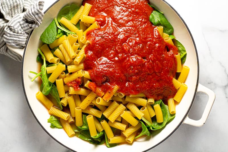 Overhead shot of a baking dish filled with fresh spinach leaves uncooked noodles and spaghetti sauce