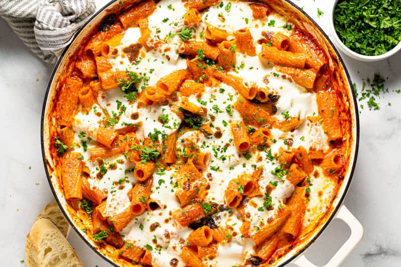 Overhead shot of a round baking dish filled with baked pasta garnished with fresh parsley