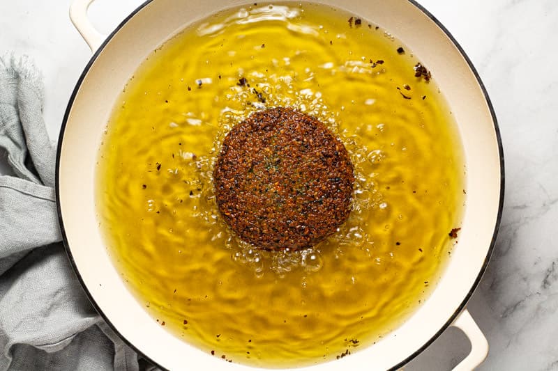 A large white pan of hot oil with a vegan falafel burger patty frying in it
