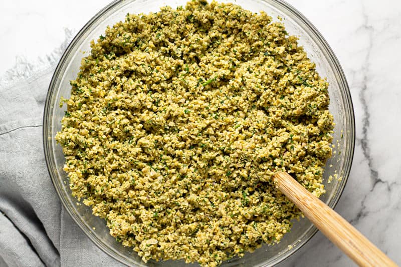 Large glass bowl filled with minced herbs and minced chickpeas mixed together
