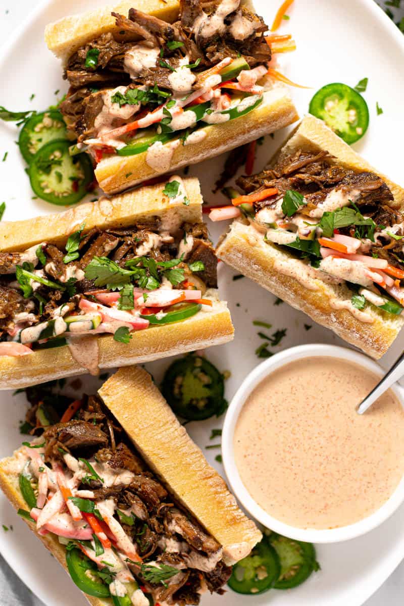 Overhead shot of a white platter filled with banh mi garnished with pickled veggies