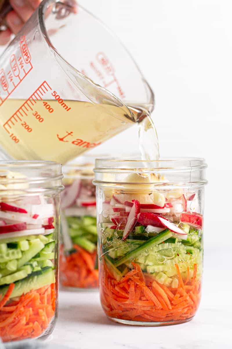Pickling liquid being poured from a large measuring cup into a mason jar of veggies 