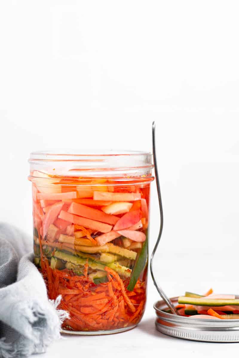 Close up shot of a jar of pickled veggies with a gray linen and a fork next to it 
