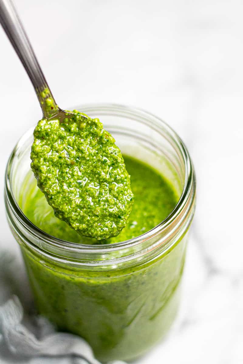 Close up shot of a small mason jar with a spoon scooping homemade spinach pesto 