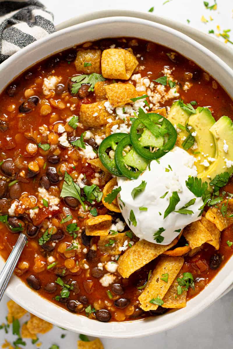Overhead shot of a bowl of vegan black bean chili garnished with Fritos and sour cream 