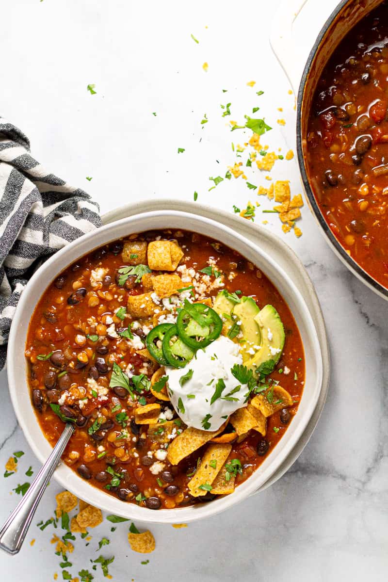 Overhead shot of a bowl of vegan black bean chili garnished with Fritos and sour cream 