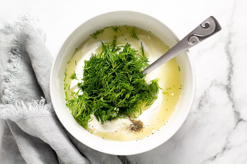 Small white bowl filled with ingredients to make dill yogurt sauce