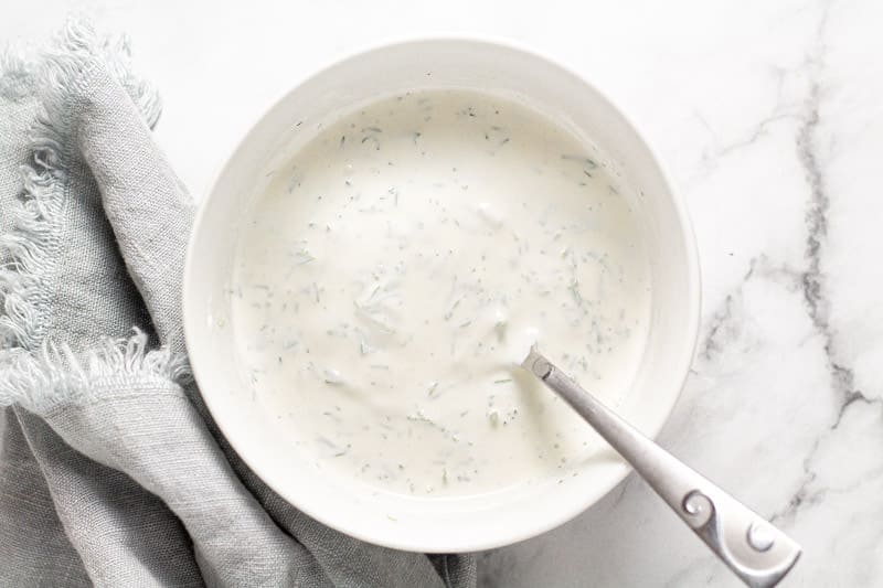 Small white bowl filled with ingredients to make dill yogurt sauce