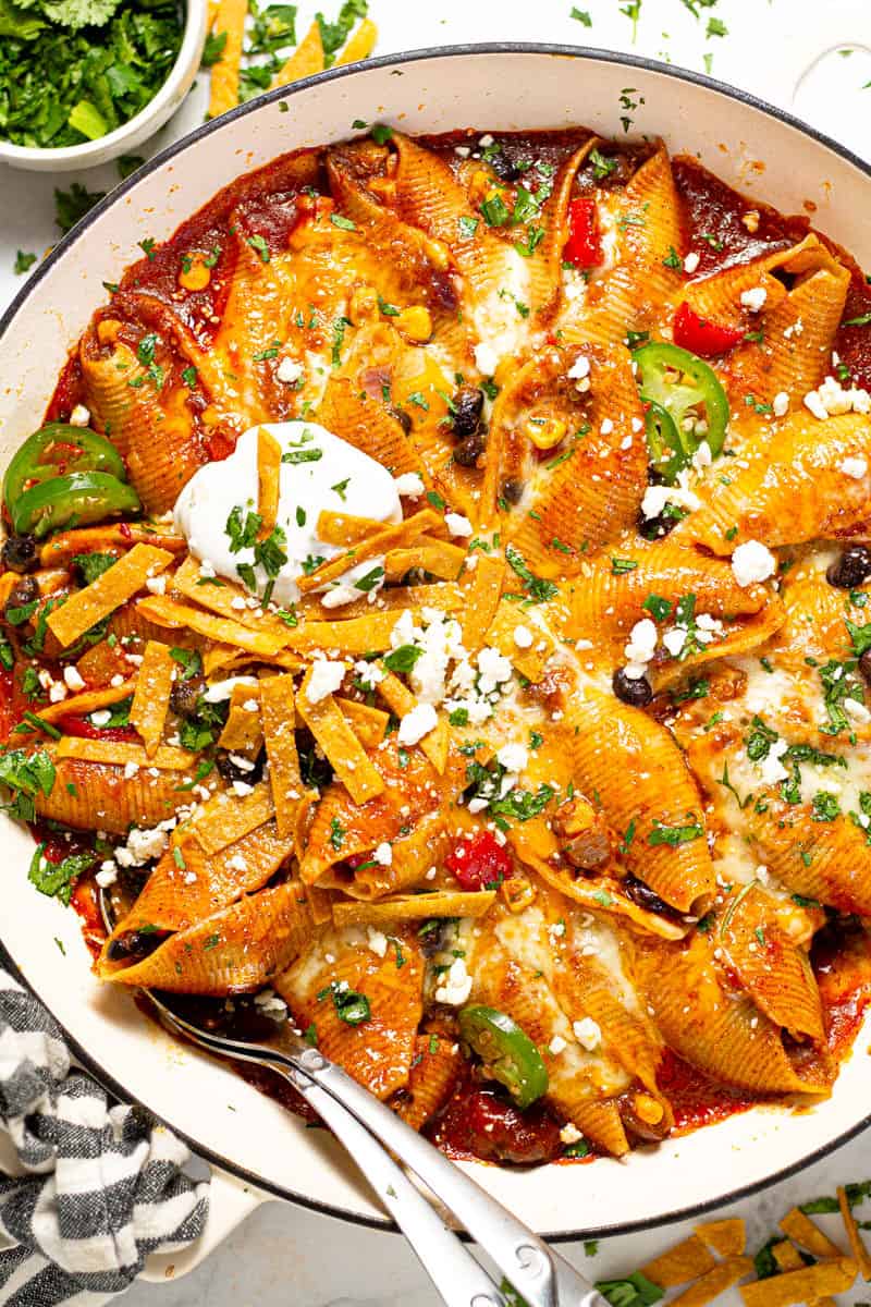 Overhead shot of a large white pan filled with Mexican stuffed shells garnished with sour cream and fresh cilantro