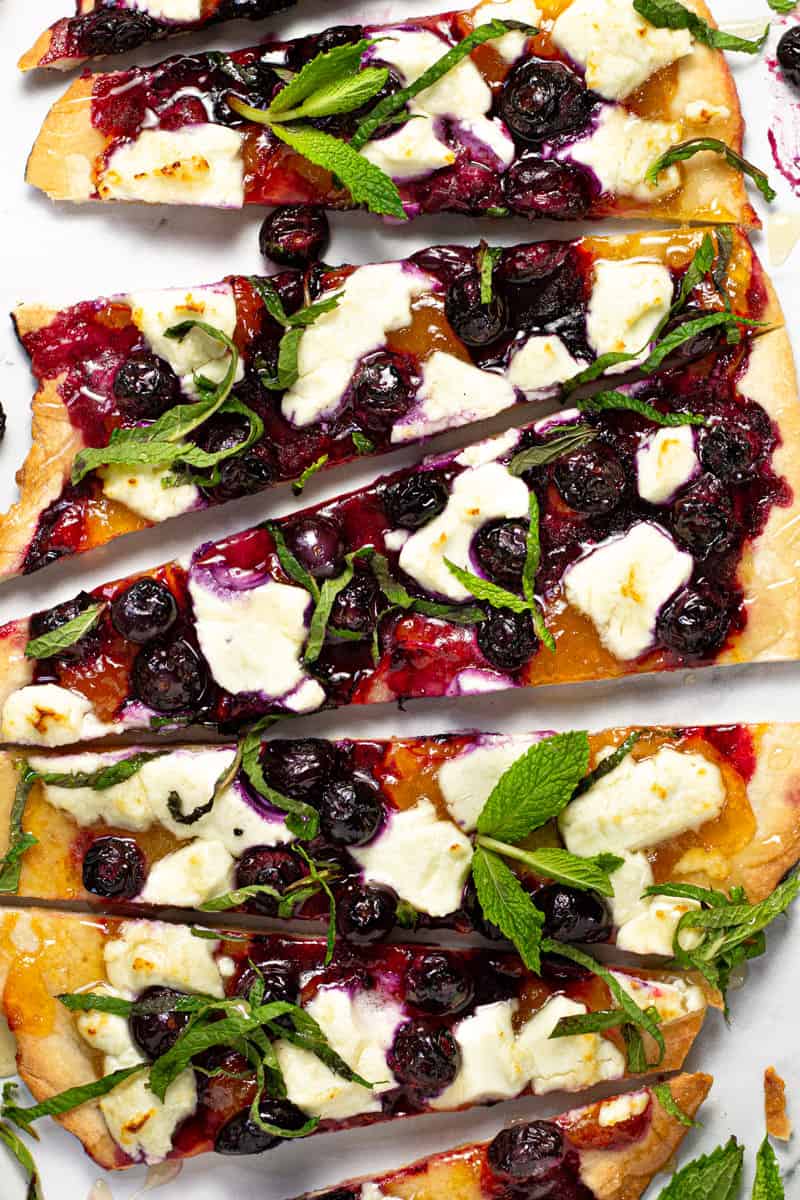 Overhead shot of a homemade blueberry goat cheese flatbread garnished with fresh mint leaves