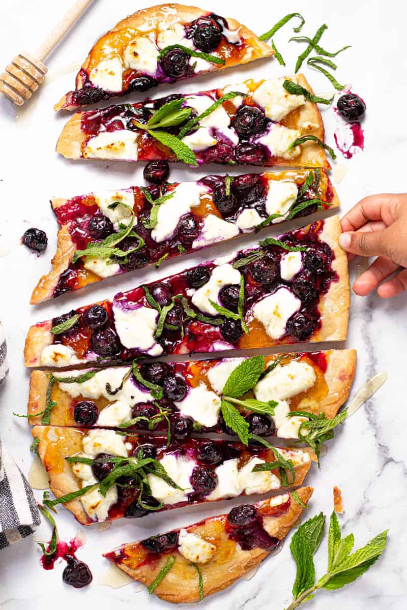 Overhead shot of a homemade blueberry goat cheese flatbread garnished with fresh mint leaves